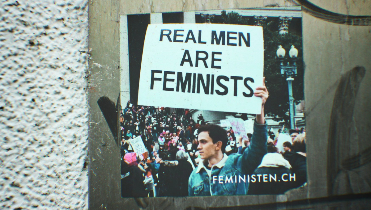 Un manifestante tiene in mano un cartello con scritto: Real men are feminists.